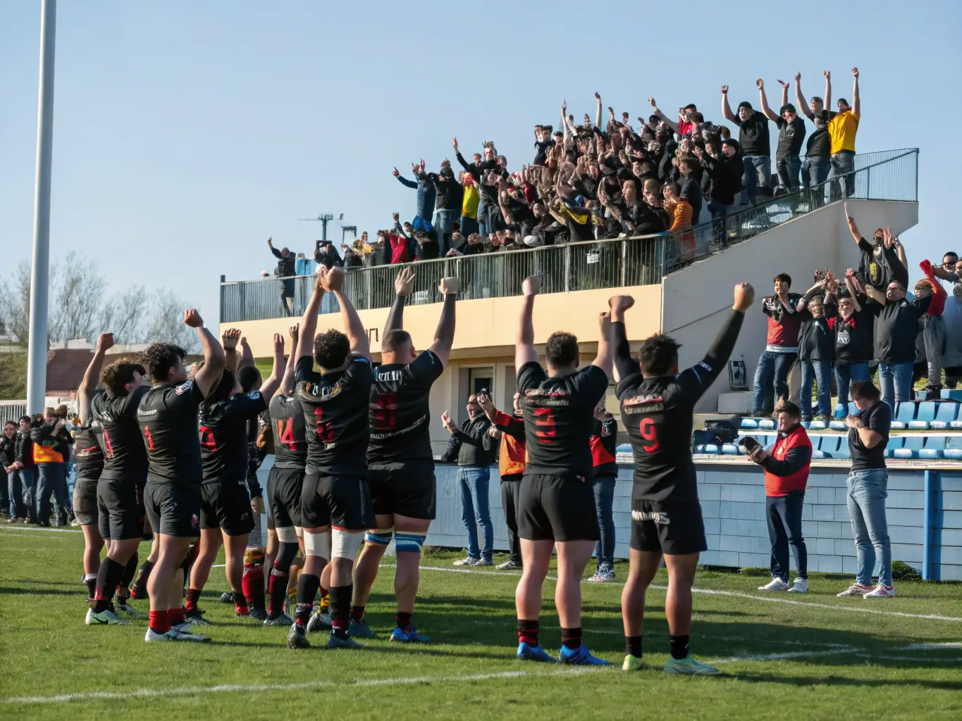 A group photo of rugby players celebrating a victory, emphasizing the sense of camaraderie and teamwork within the OLYMPIC RUGBY CLUB RIOM ES MONTAGNE. The players are smiling and cheering, with arms around each other.